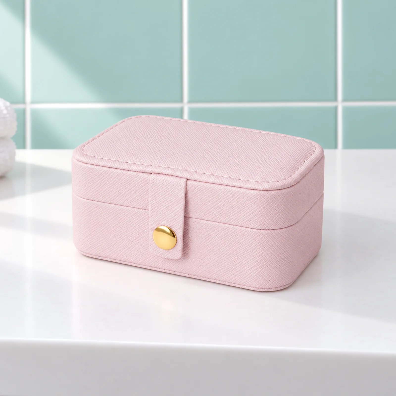 Mini boîte à bijoux de voyage, rose pâle, fermée de trois quarts sur la tablette blanche