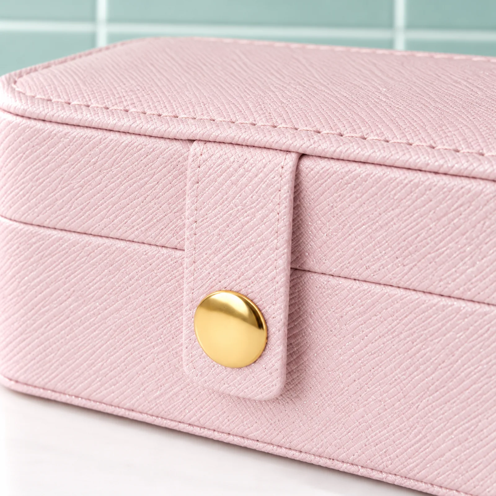 Mini boîte à bijoux de voyage rose pâle, détail de la languette fermée, du bouton pression doré rond et du simili cuir finement pailleté